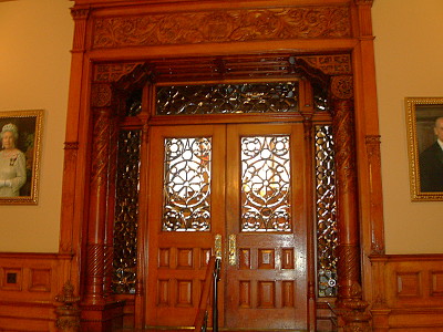 [A wooden structure borders a small alcove with wooden columns. The doors are wood and the window in the doors and around the doors are stained glass.]